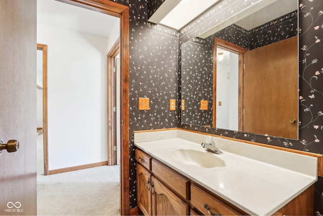 bathroom with wallpapered walls, vanity, and baseboards