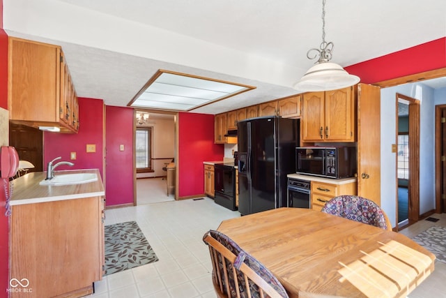 kitchen with brown cabinetry, a sink, black appliances, light countertops, and under cabinet range hood