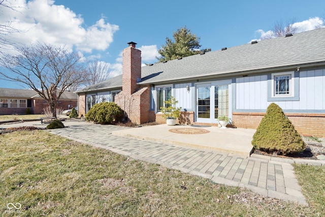 back of property with brick siding, a chimney, a lawn, a patio area, and board and batten siding