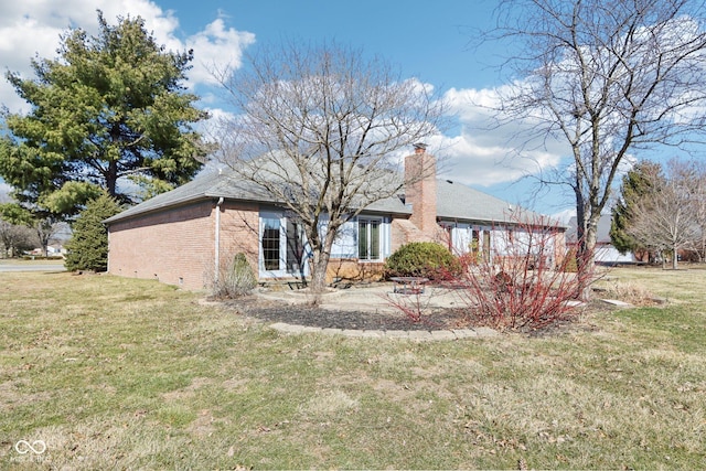 back of house featuring a yard, brick siding, and a chimney