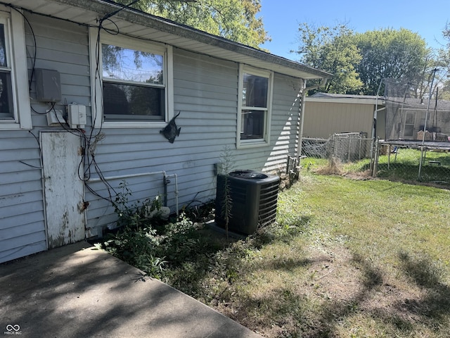 view of side of home with a yard, a trampoline, cooling unit, and fence