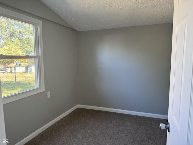 unfurnished room with dark colored carpet, lofted ceiling, baseboards, and a textured ceiling