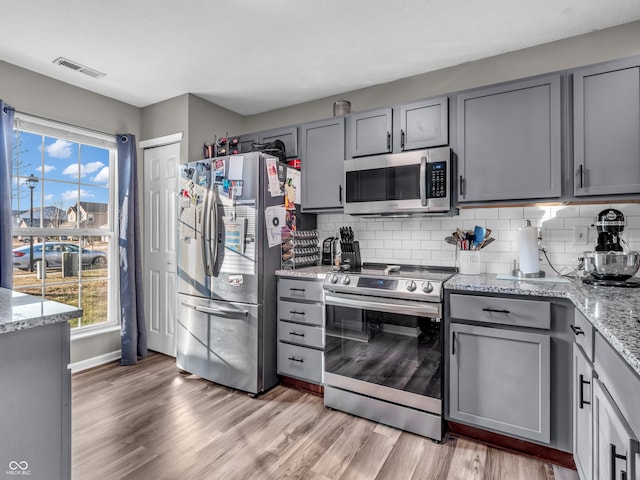 kitchen with visible vents, light wood-style flooring, gray cabinets, stainless steel appliances, and tasteful backsplash