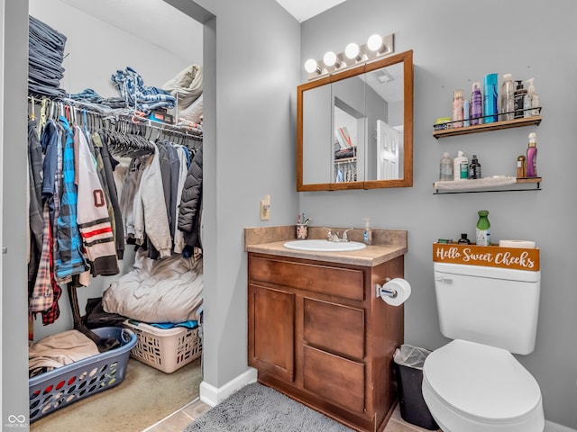 bathroom with a spacious closet, toilet, vanity, and baseboards