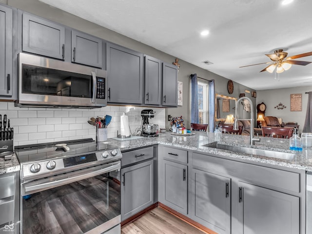 kitchen featuring light wood-style flooring, gray cabinets, a sink, decorative backsplash, and appliances with stainless steel finishes