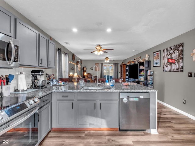 kitchen with gray cabinets, a sink, tasteful backsplash, stainless steel appliances, and a peninsula