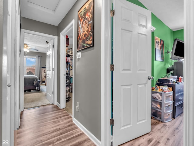 hall with baseboards, attic access, and wood finished floors