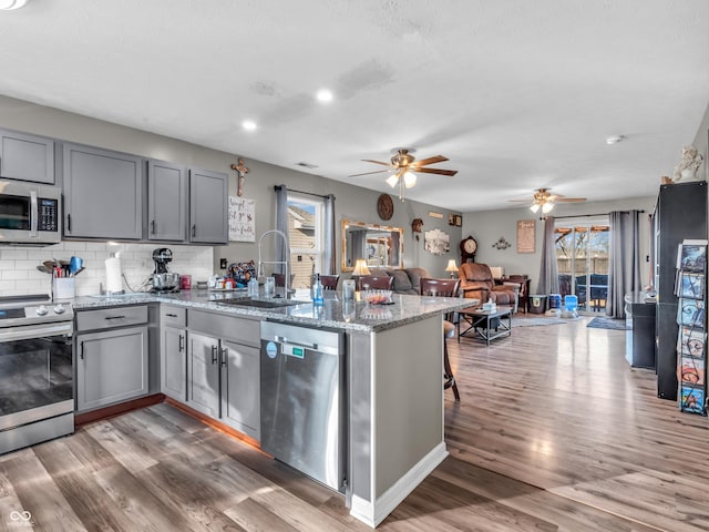 kitchen featuring a peninsula, gray cabinets, a sink, appliances with stainless steel finishes, and tasteful backsplash