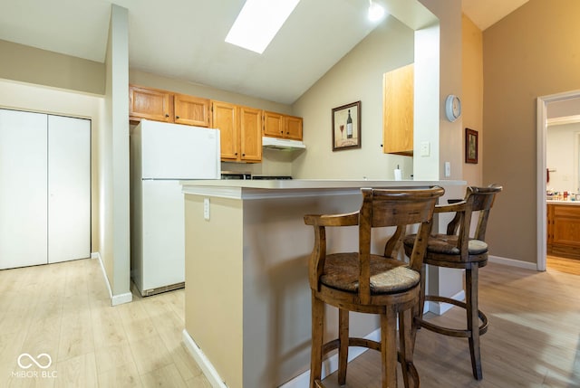 kitchen with a breakfast bar, vaulted ceiling with skylight, light wood-type flooring, and freestanding refrigerator