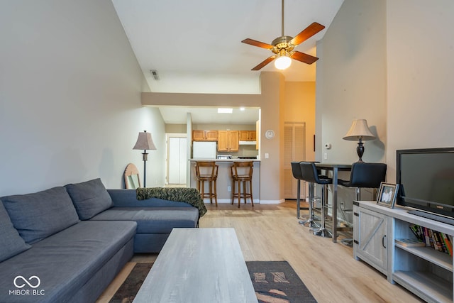 living room with visible vents, light wood-style flooring, a ceiling fan, a high ceiling, and baseboards