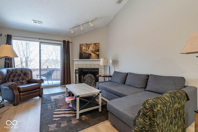 living room with wood finished floors, visible vents, a fireplace, vaulted ceiling, and rail lighting