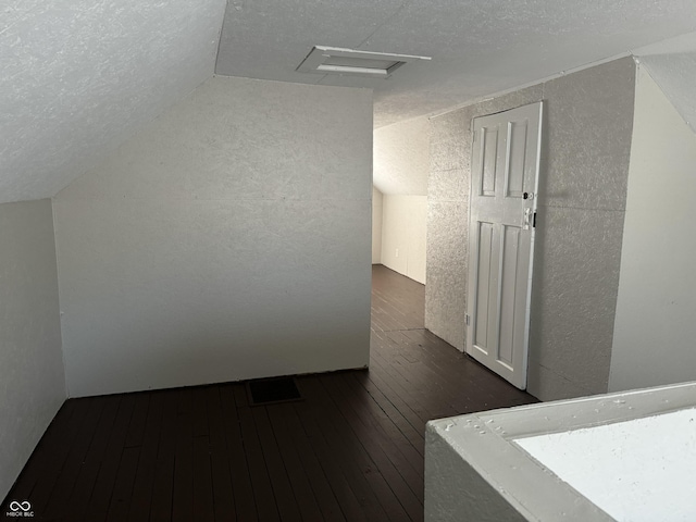 additional living space with attic access, a textured wall, wood-type flooring, vaulted ceiling, and a textured ceiling