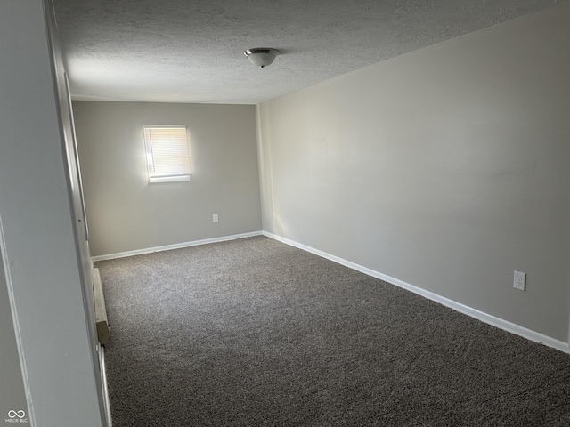 spare room with a textured ceiling, dark colored carpet, and baseboards