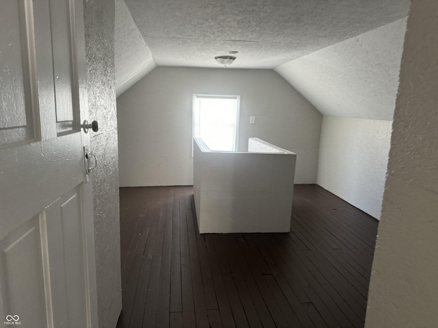 bonus room featuring a textured ceiling, a textured wall, dark wood-type flooring, and vaulted ceiling