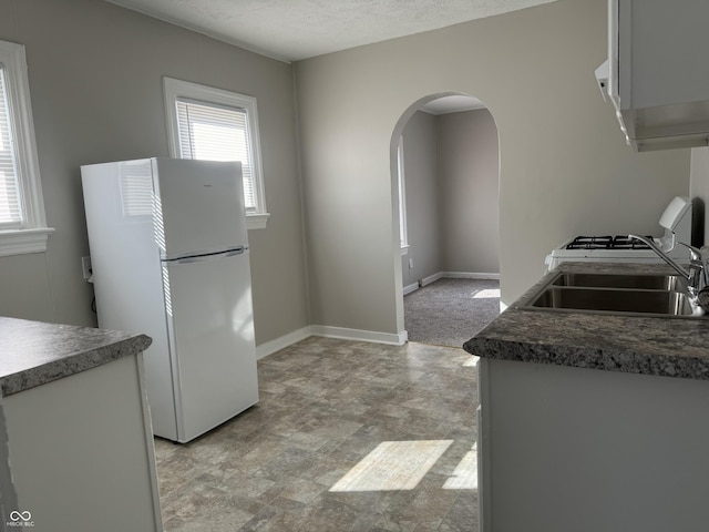 kitchen featuring arched walkways, white appliances, a sink, and a wealth of natural light