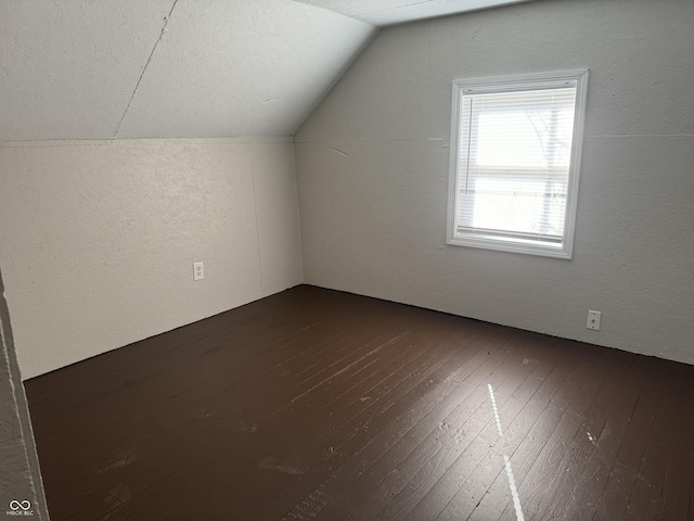 bonus room with dark wood-style floors, vaulted ceiling, and a textured wall