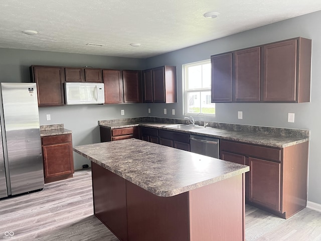 kitchen featuring light wood-style flooring, a center island, dark countertops, appliances with stainless steel finishes, and a sink