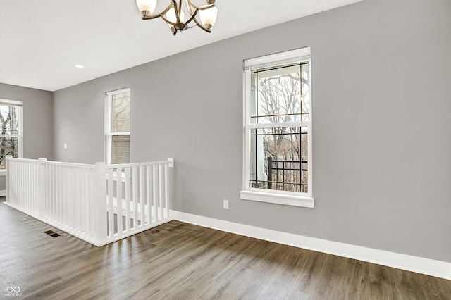 spare room with baseboards, visible vents, a chandelier, and wood finished floors