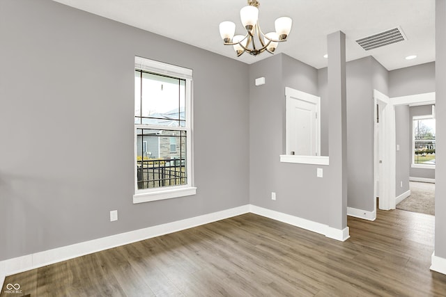 empty room featuring baseboards, visible vents, a notable chandelier, and wood finished floors