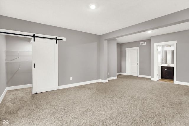 unfurnished bedroom with a barn door, visible vents, baseboards, carpet, and ensuite bath