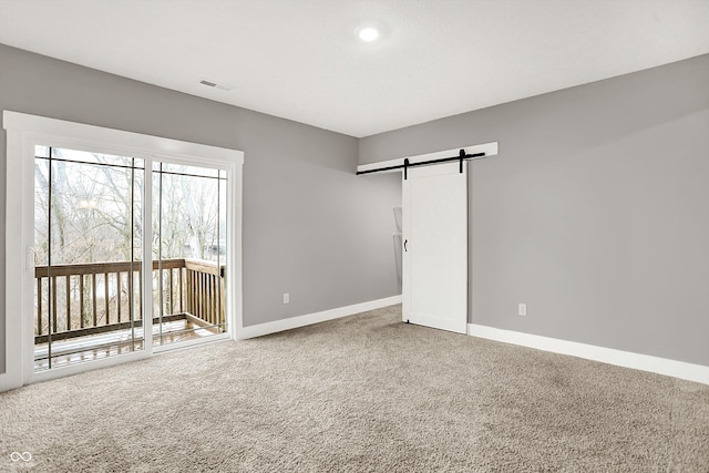 unfurnished room with a barn door, visible vents, baseboards, and carpet flooring