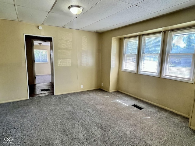 carpeted spare room with a drop ceiling, visible vents, and baseboards