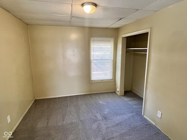 unfurnished bedroom with a paneled ceiling, baseboards, carpet floors, and a closet