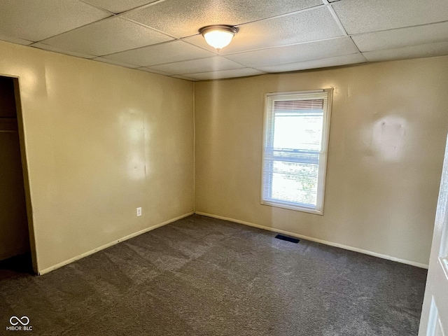 empty room featuring a paneled ceiling, baseboards, visible vents, and dark carpet