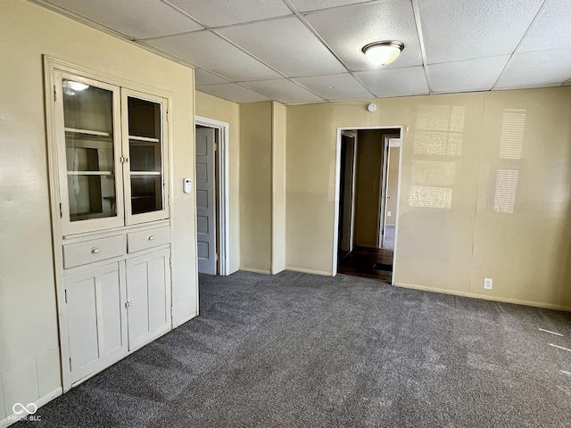 unfurnished room with dark colored carpet and a drop ceiling