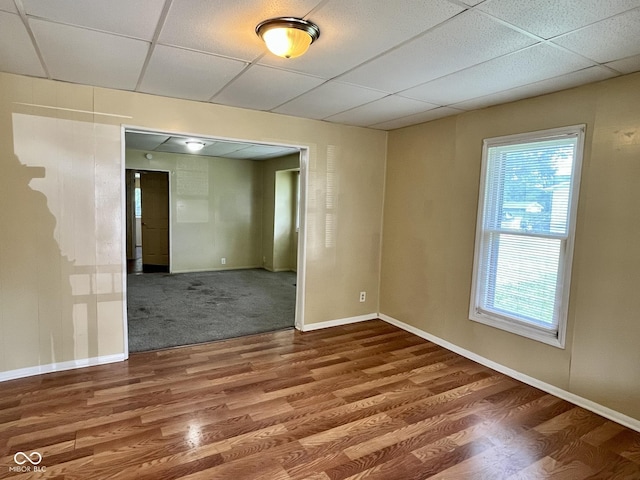 empty room featuring a drop ceiling, baseboards, and wood finished floors