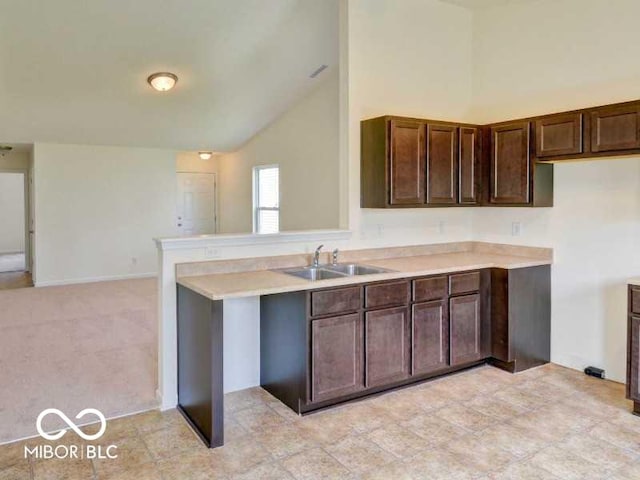 kitchen with dark brown cabinetry, a peninsula, light countertops, high vaulted ceiling, and a sink