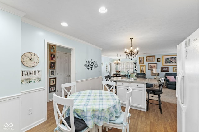 dining room featuring light wood finished floors, wainscoting, ornamental molding, a chandelier, and recessed lighting