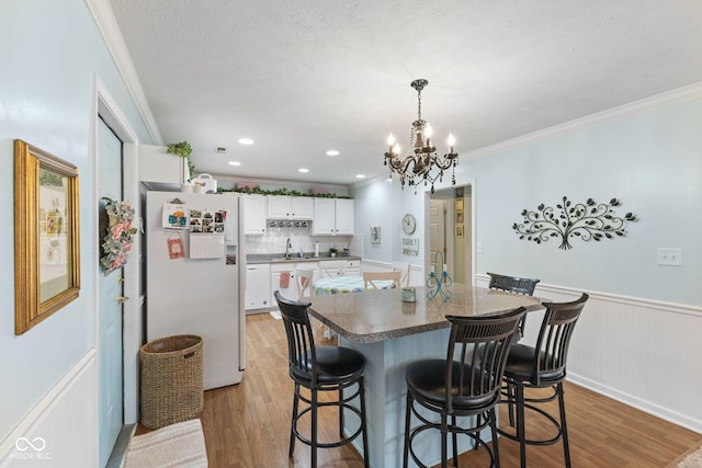 kitchen featuring light wood-style flooring, ornamental molding, wainscoting, freestanding refrigerator, and a center island