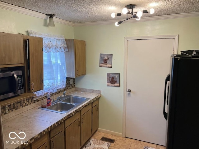 kitchen with a sink, visible vents, freestanding refrigerator, stainless steel microwave, and crown molding