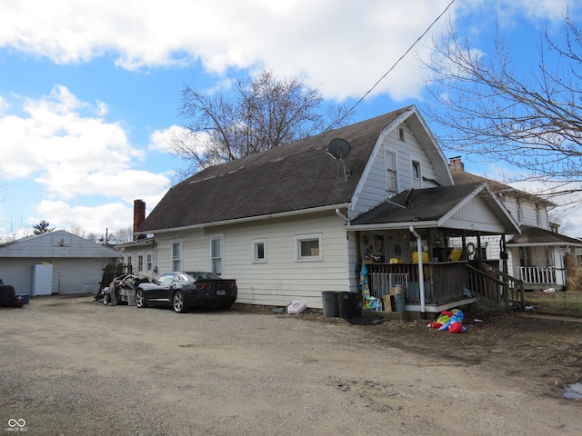 view of side of property featuring a porch, a garage, a shingled roof, a gambrel roof, and driveway