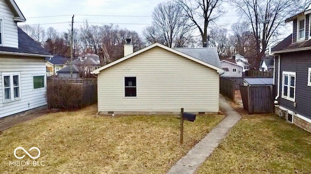 view of side of property with fence, a yard, a chimney, an outdoor structure, and crawl space