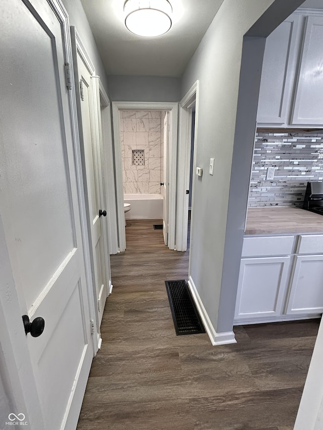 hallway with dark wood finished floors, visible vents, and baseboards