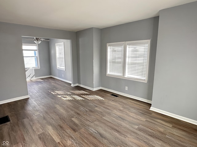 spare room featuring dark wood-type flooring, a ceiling fan, visible vents, and baseboards