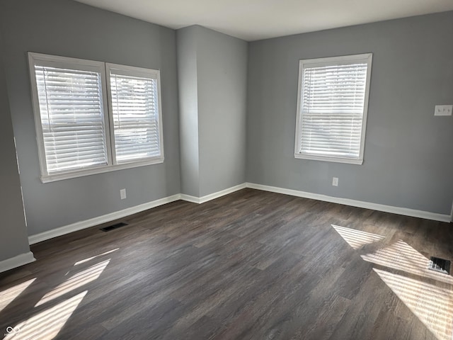 spare room featuring dark wood-type flooring, a wealth of natural light, and visible vents