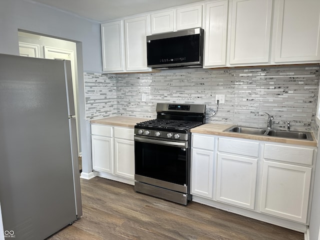 kitchen featuring tasteful backsplash, butcher block counters, dark wood-style flooring, stainless steel appliances, and a sink