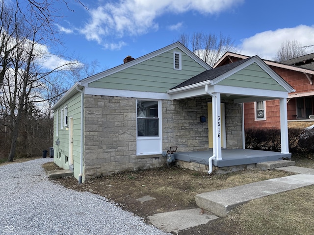 view of front facade with stone siding, a porch, and a chimney