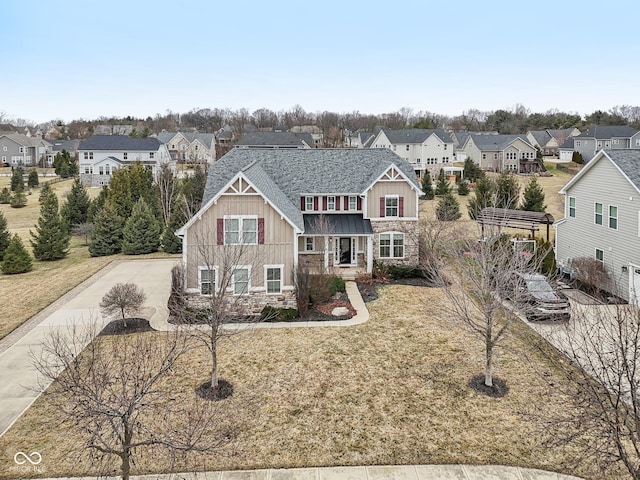 view of front of home featuring driveway, a residential view, a front lawn, stone siding, and board and batten siding