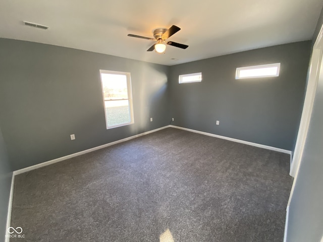 empty room with dark carpet, visible vents, ceiling fan, and baseboards