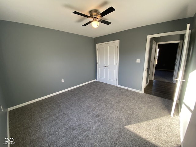 unfurnished bedroom with dark colored carpet, a closet, a ceiling fan, and baseboards