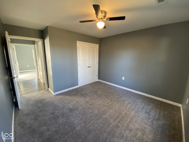 unfurnished bedroom with ceiling fan, dark colored carpet, a closet, and baseboards