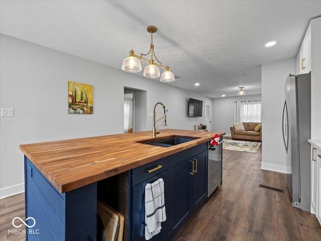 kitchen with blue cabinetry, appliances with stainless steel finishes, open floor plan, a sink, and wood counters