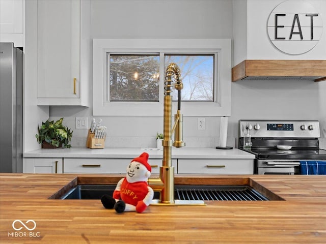 kitchen featuring appliances with stainless steel finishes, white cabinetry, wooden counters, and ventilation hood