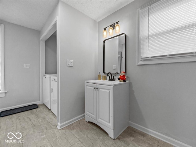 bathroom with a textured ceiling, vanity, baseboards, washer and clothes dryer, and plenty of natural light