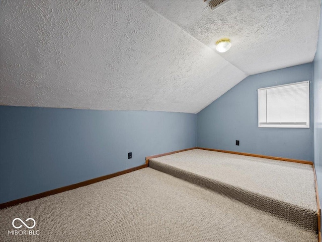 additional living space with carpet flooring, vaulted ceiling, a textured ceiling, and baseboards