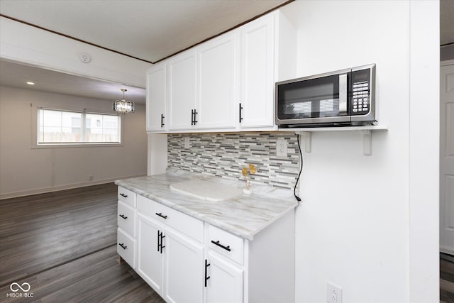 kitchen featuring white cabinets, decorative backsplash, stainless steel microwave, dark wood-style flooring, and light stone countertops